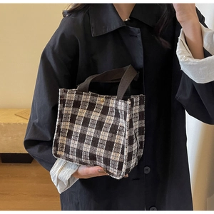 Close-up of small checkered tote bag with brown woven handles and gold snap button detail