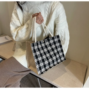 Close-up of woven checkered tote bag with rope handles held by a model in knitwear
