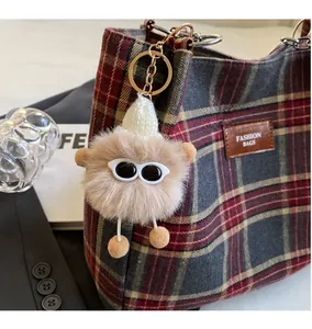 Detail view of a cute fuzzy keychain with sunglasses on a stylish plaid tote bag