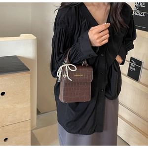 Detail of dark brown crocodile pattern handbag with pearl bow charm and brand logo