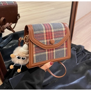 Detail of checkered crossbody bag with V-shaped flap and plush doll charm in mirror reflection