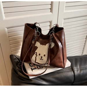Detail of a brown tote bag with a cartoon rabbit print and silver chain strap on a sofa