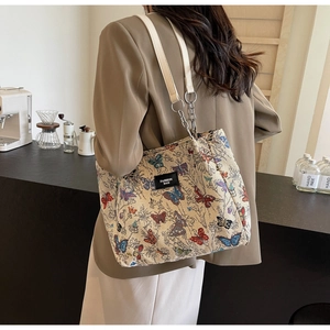 Detail of beige tote bag with butterfly print and metal chain strap in cafe setting