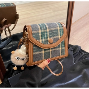 Detail of vintage plaid crossbody bag with brown leather trim and cute plush doll charm