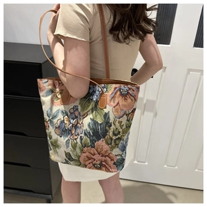 Dettaglio borsa tote floreale con manici in pelle marrone indossata sulla spalla