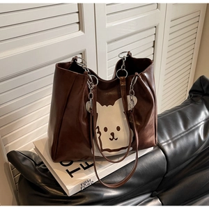 Close-up of brown tote bag featuring white cartoon prints and silver metal chain strap