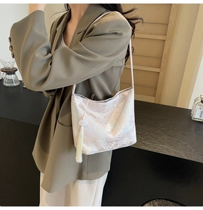 Dettaglio della borsa a secchiello in jacquard rosa con tracolla fine e nappa bianca