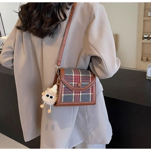 Detail of vintage plaid crossbody bag with brown leather trim and cute plush monster charm