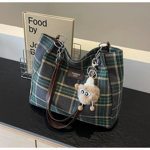 Detail view of plaid tote bag featuring leather straps, metal chains, and plush charm