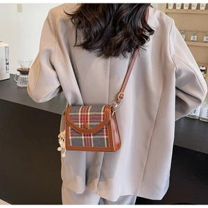 Close-up of retro plaid crossbody bag with brown leather trim and plush charm detail