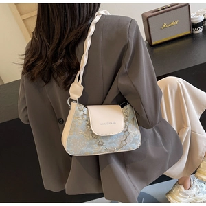 Détail du sac porté épaule en jacquard bleu avec bandoulière tressée et chaîne fleur