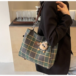 Detail of green plaid tote bag with plush charm and chain strap on female shoulder