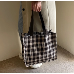 Close-up of the woven plaid wool texture and sturdy brown handle of this tote bag