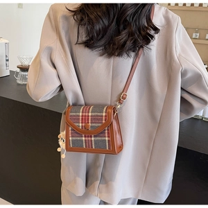 Close-up of retro plaid crossbody bag with brown leather trim and plush bear charm