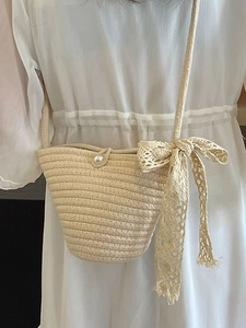 Beige handwoven straw crossbody bag with pearl button and lace bow accent on model