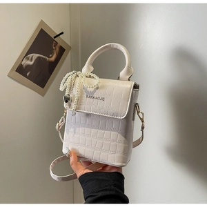 Detail of white crocodile texture mini bag with pearl bow and heart pendant