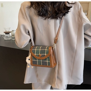 Brown leather and green plaid crossbody bag with sheep pendant shown on model in cafe