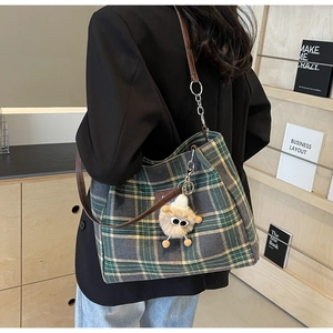 Detail of dark green plaid canvas tote bag with leather strap and plush doll pendant