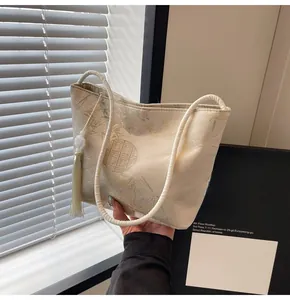 Dettaglio borsa a secchiello in broccato beige con motivi tradizionali e nappine bianche