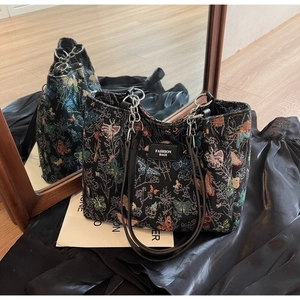 Detail of black jacquard tote bag featuring colorful butterfly embroidery and metal chains