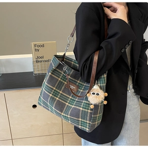 Detail of plaid tote bag with brown leather straps and fuzzy charm for daily commute