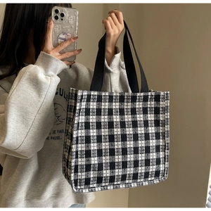 Detailed close-up of a black and white checkered tweed tote bag with woven handles