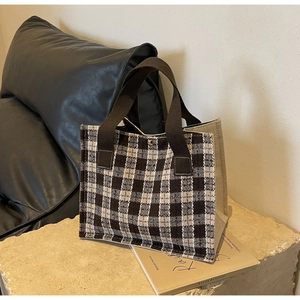 Detail of checkered canvas tote bag with brown woven handles and metal snap closure