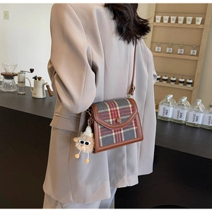 Detail of plaid crossbody bag with brown leather trim and plush monster charm pendant