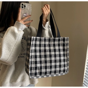 Detail of checkered canvas tote bag with black webbing straps held by a model