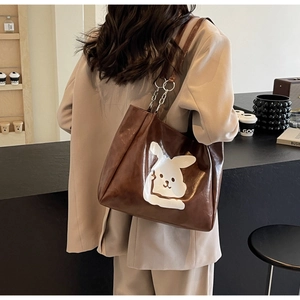 Detail of a large brown PU tote bag with a white cartoon rabbit and metal chain strap