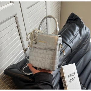 Detailed close-up of silver crocodile pattern handbag with pearl heart pendant charm