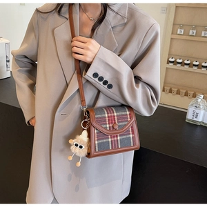Detail of retro plaid crossbody bag with leather trim and plush eyeball charm accessory