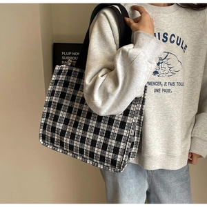 Side view of a black and white plaid tweed tote bag with wide black canvas shoulder straps