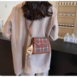 Detail of vintage plaid crossbody bag featuring leather trim and a cute plush charm