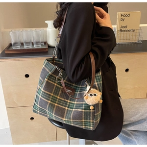 Detail of green and grey plaid tote bag with brown leather strap and furry charm