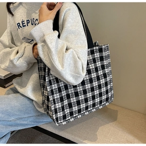 Close-up of black and white checkered tote bag with woven strap on shoulder