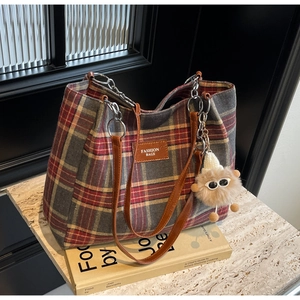 Close-up of red and grey plaid tote bag with leather straps and plush toy charm