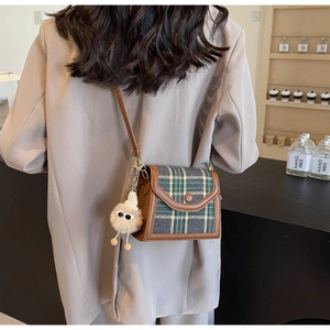 Detail of plaid tweed crossbody bag with brown leather trim and fuzzy monster charm