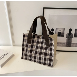 Detail of plaid fabric tote bag with brown handles and a gold metal snap button closure