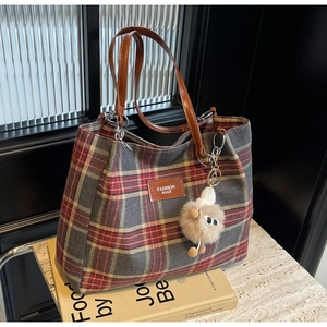 Detail of checkered tote bag with brown leather handles and plush monster charm decoration