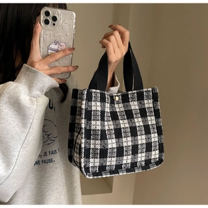 Detail of checkered tote bag with tweed texture, black handle and gold metal button