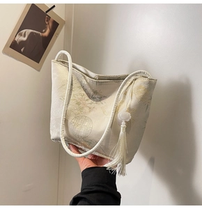 Dettaglio della borsa a secchiello in jacquard beige con motivi floreali e nappa bianca