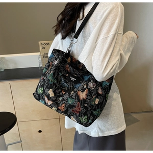 Close-up of black canvas tote bag with colorful butterfly embroidery and leather strap
