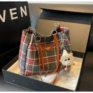 Detail of red plaid tote bag with brown leather straps and plush pom-pom in a gift box