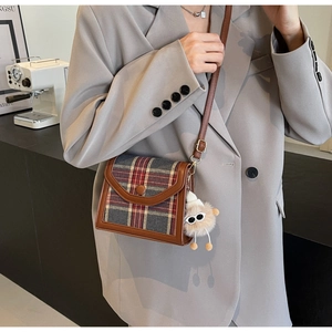 Detail of vintage plaid messenger bag with leather trim and plush doll charm