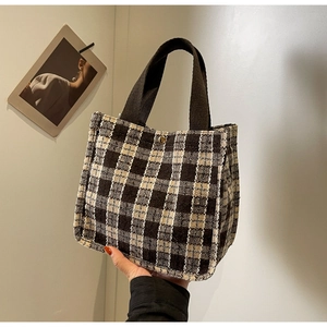 Detail of checkered tote bag showing woven texture, dark brown handles and metal buckle close-up