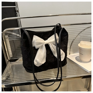 Detail of star-textured black tote bag with large white bow in a modern lifestyle setting