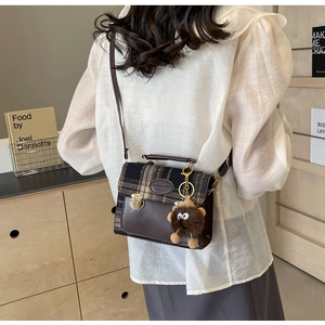 Detail of vintage brown leather and plaid crossbody bag with a plush monster pendant