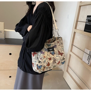 Detail of cream tote bag with colorful butterfly patterns and metal chain shoulder strap