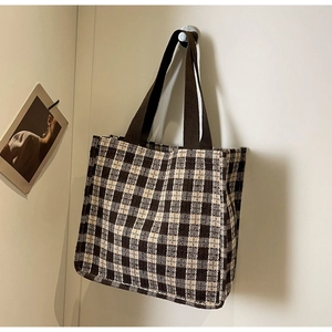 Detail of checkered canvas tote bag showing the texture and brown woven strap on a hook